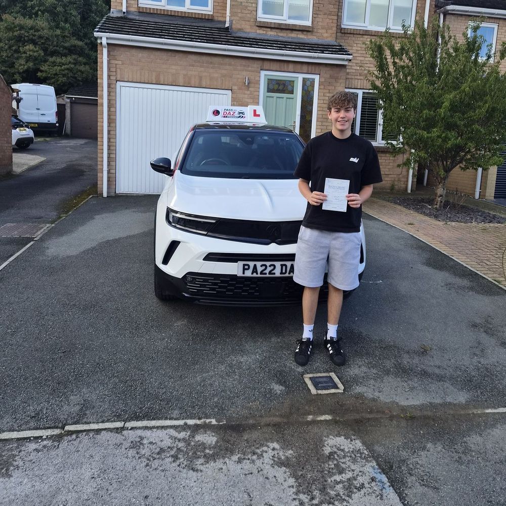 Young man holding his driving test pass certificate in front of the Pass with Daz tuition car